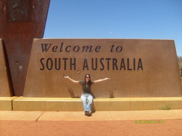 Meg Rouje sitting in front of the monument "Welcome to South Australia"