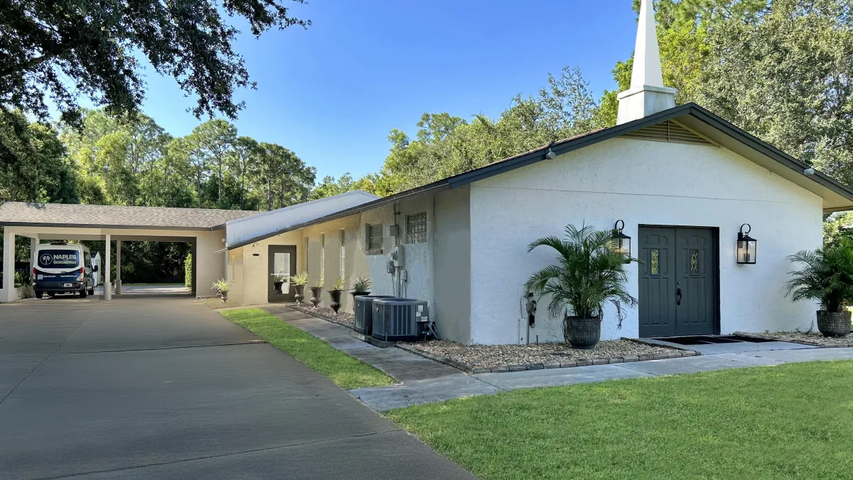 The church from Autumn Oaks Lane: a white building with a steeple, a covered carport to the left, and dark double doors at the front entrance.
