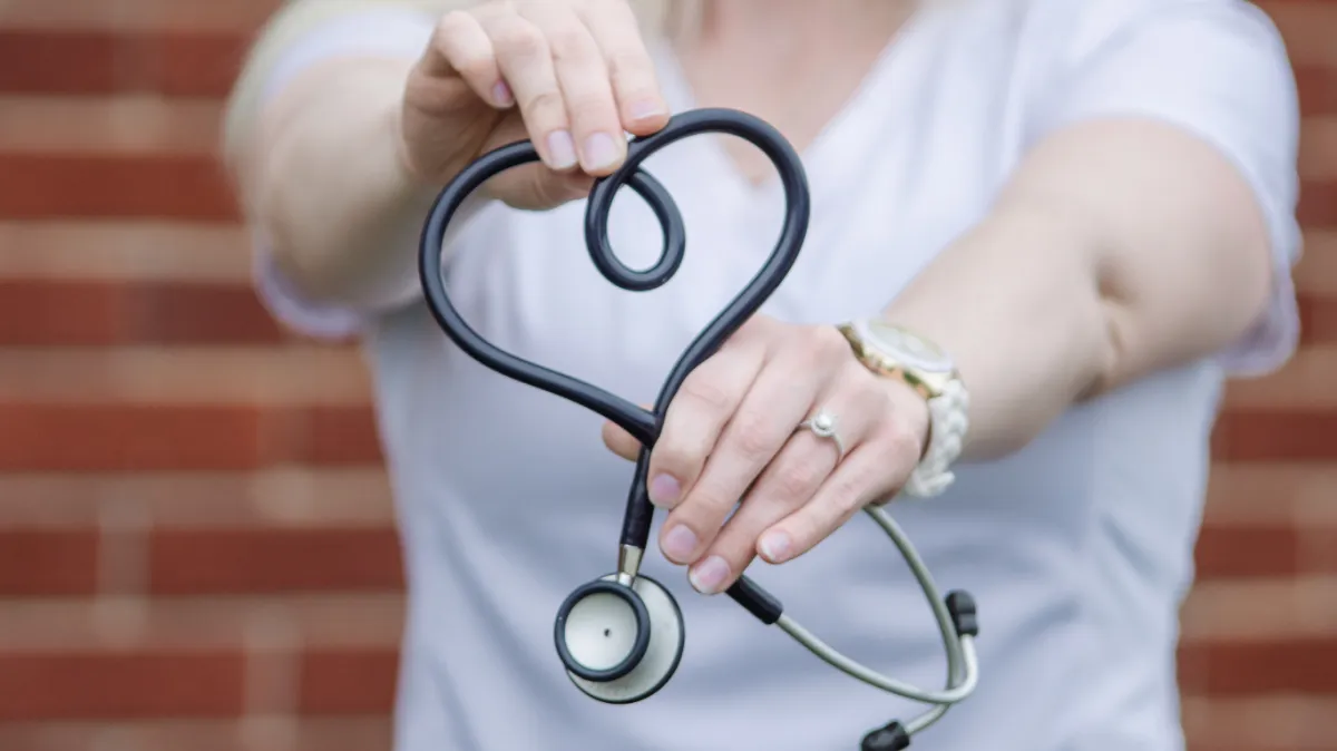 Healthcare professional holding a stethoscope shaped into a heart, symbolizing compassionate care.