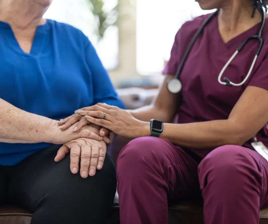 Healthcare provider in scrubs comforting a patient by holding their hands.