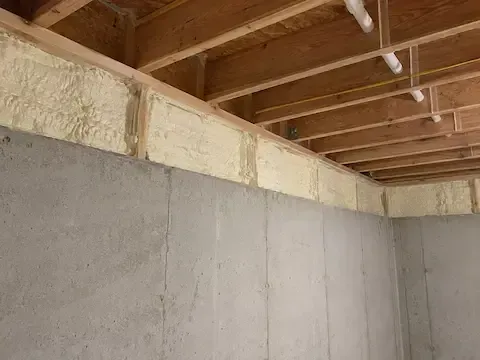 Rim joists sealed with spray foam above a poured concrete basement wall in Perth Amboy