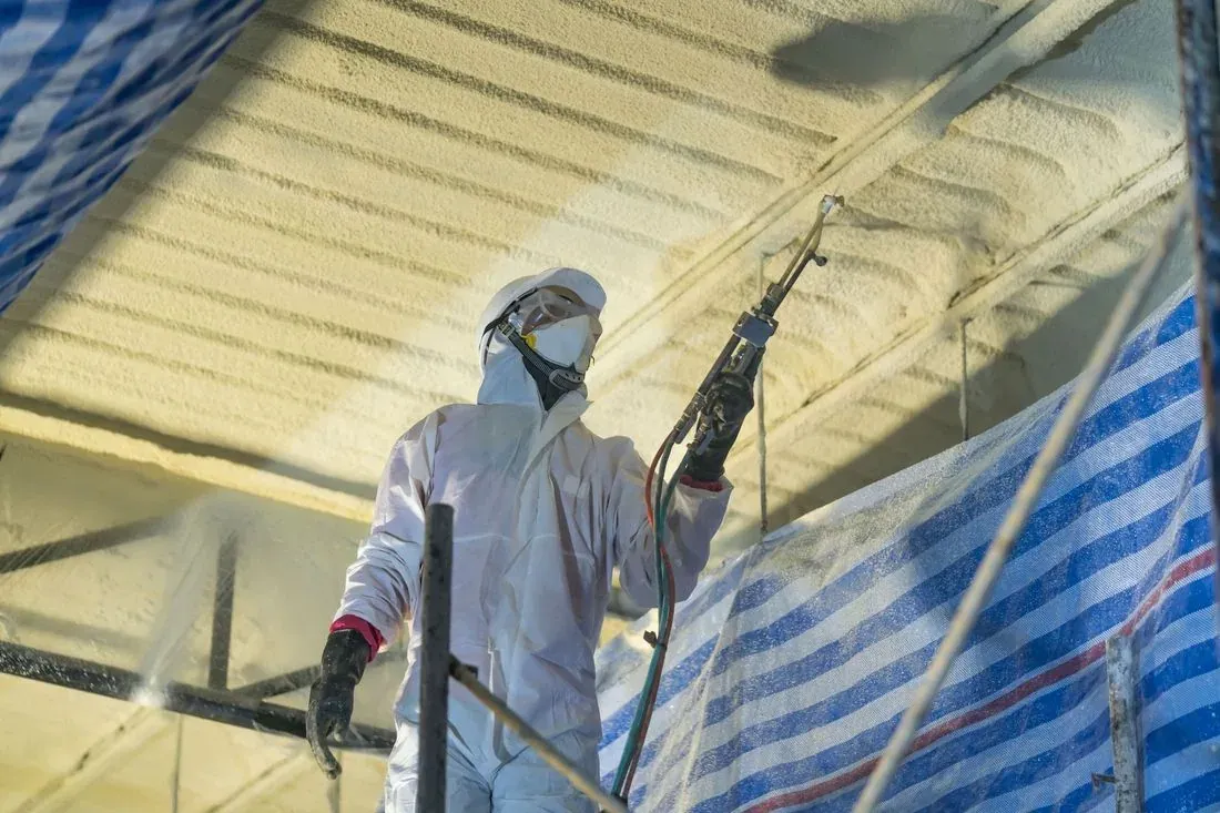 Crew member on scaffolding spraying foam insulation across a warehouse ceiling with Perth Amboy Spray Foam Insulation
