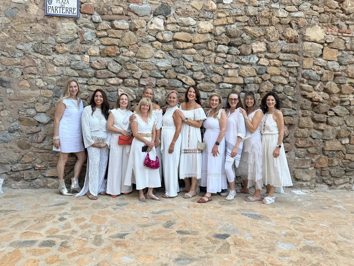 Naomi Morgan with a group of coaches she has trained, all dressed in white, in front of a stone wall in Spain