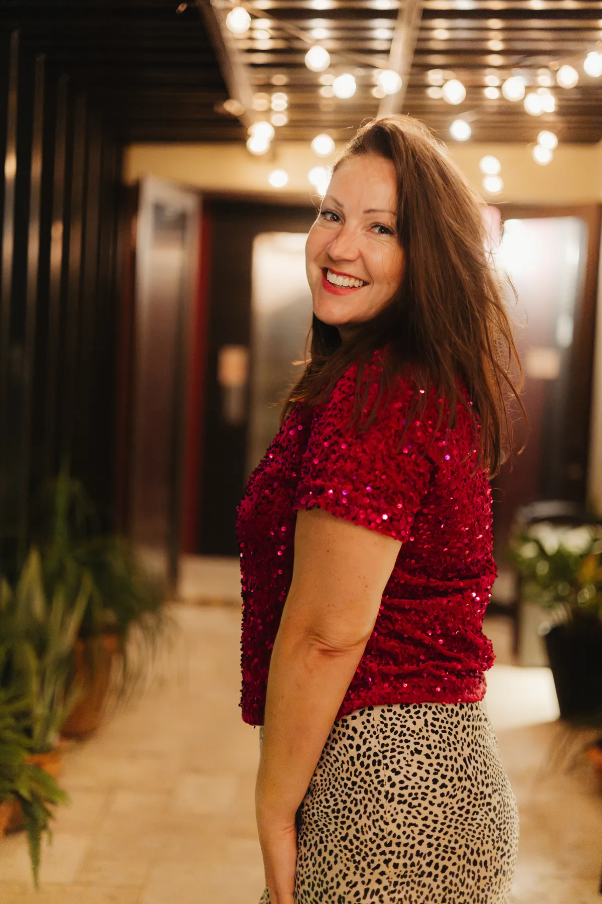 Naomi Morgan smiling over her shoulder in a red sequinned top