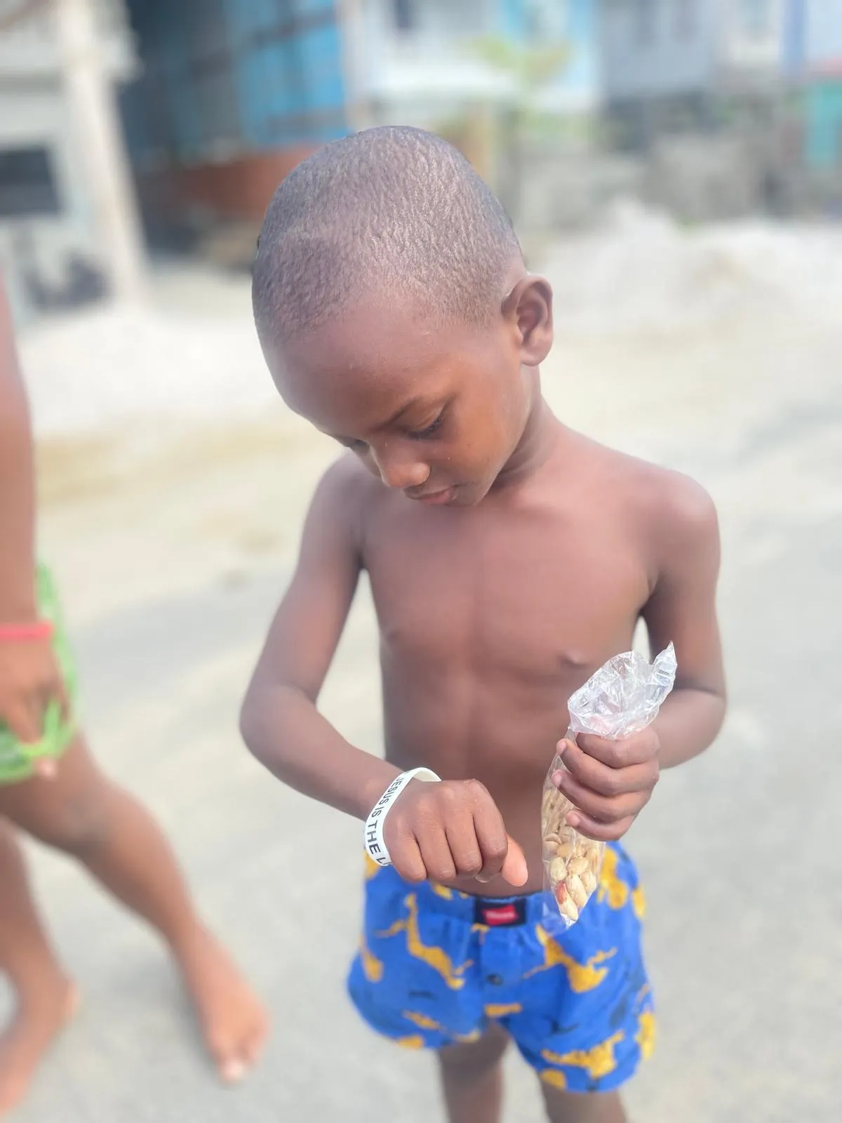 A boy wearing a Jesus Is The wristband holding a bag of peanuts