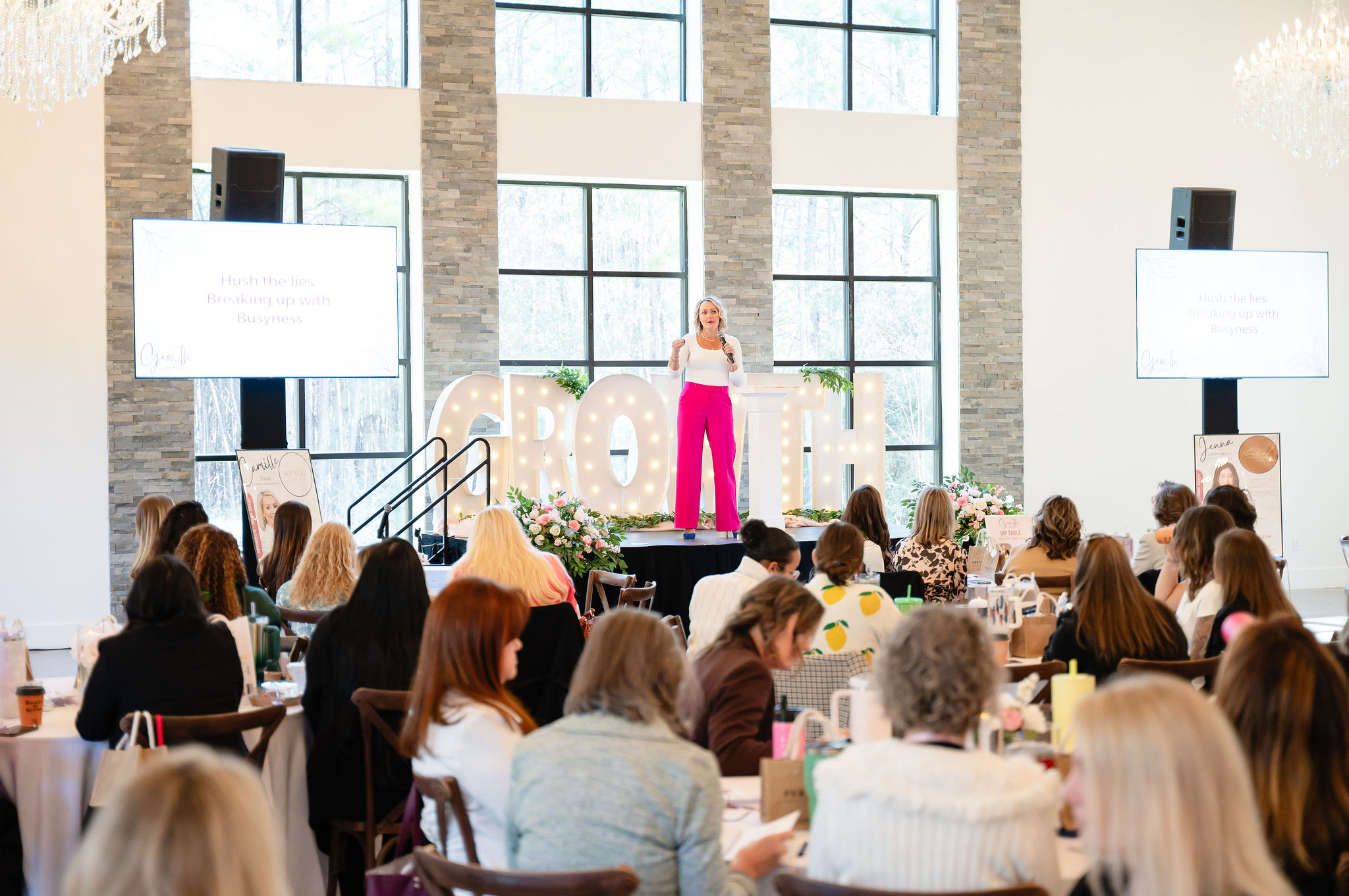 Lindsay Fletcher speaking on stage at The Growth Summit, a faith-centered women's business conference in Houston, TX. Lindsay is wearing a white shirt with hot pink pants and is holding a microphone.
