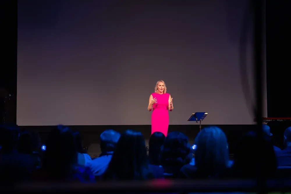 Lindsay Fletcher speaking on stage at Inspired Leaders, a local small business networking event, in The Woodlands, TX. She is wearing a magenta dress.