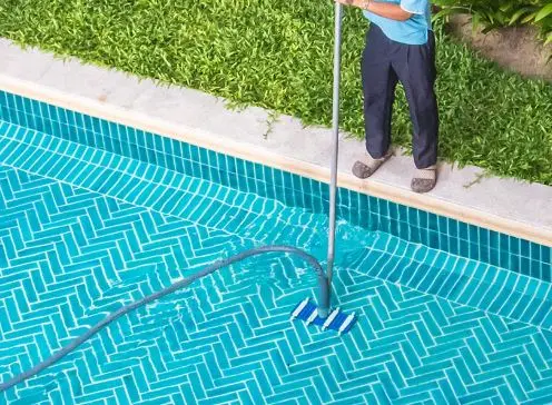 Manual vacuum cleaning debris from herringbone tile pool floor during routine maintenance