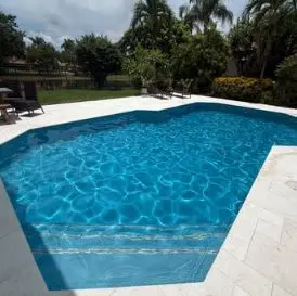 Sparkling clean freeform pool with white travertine deck after weekly service by Lakeside Pool Service