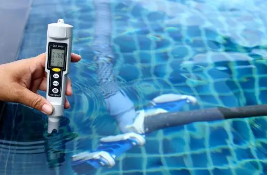 Hand holding digital salt meter to test saltwater pool chemistry during service visit