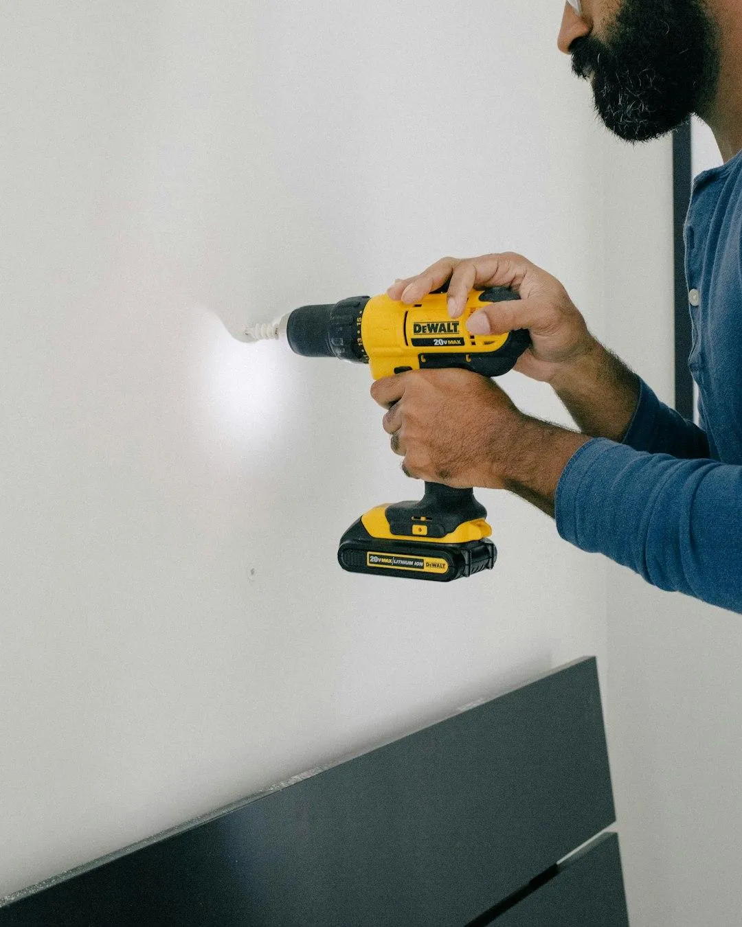 A contractor using a yellow power drill to perform precise repairs on a white wall, illustrating OneC Consulting's hands-on project coordination and 'Honey-Do List' services.