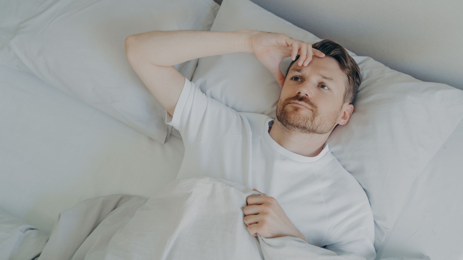 Man waking up feeling exhausted after eight hours of sleep with morning sunlight, illustrating poor sleep quality and nervous system health.