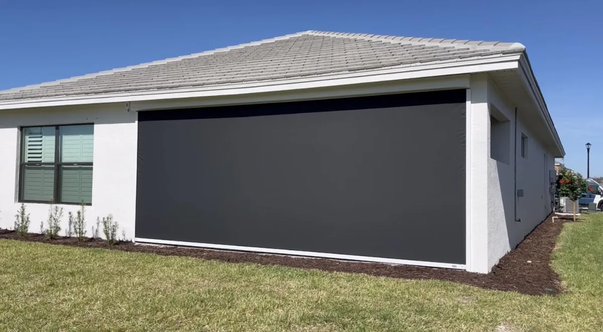 Picture of a white house with black MaganaTrack motorized screen deployed. 