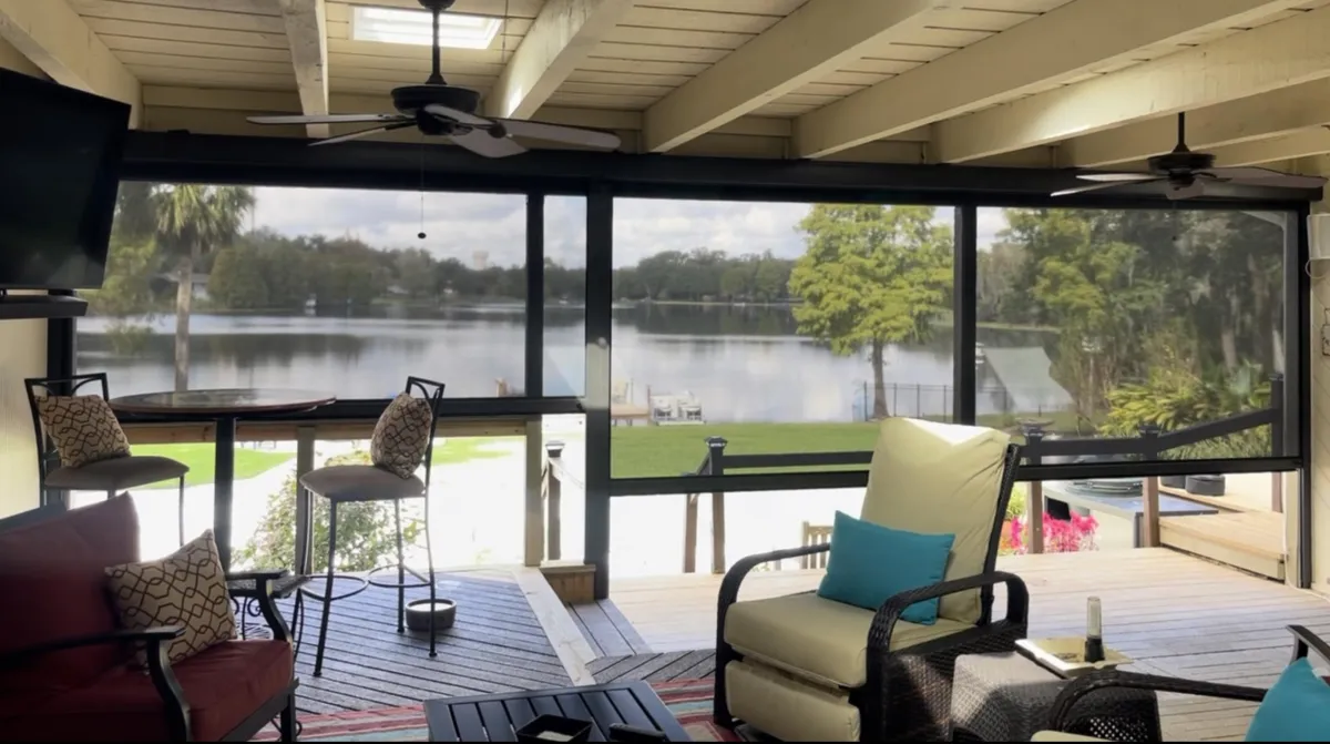 A photo of patio with nicely spaced furniture. With Retractable bug screens providing , beyond that a lake providing protection on a clear shine day. 