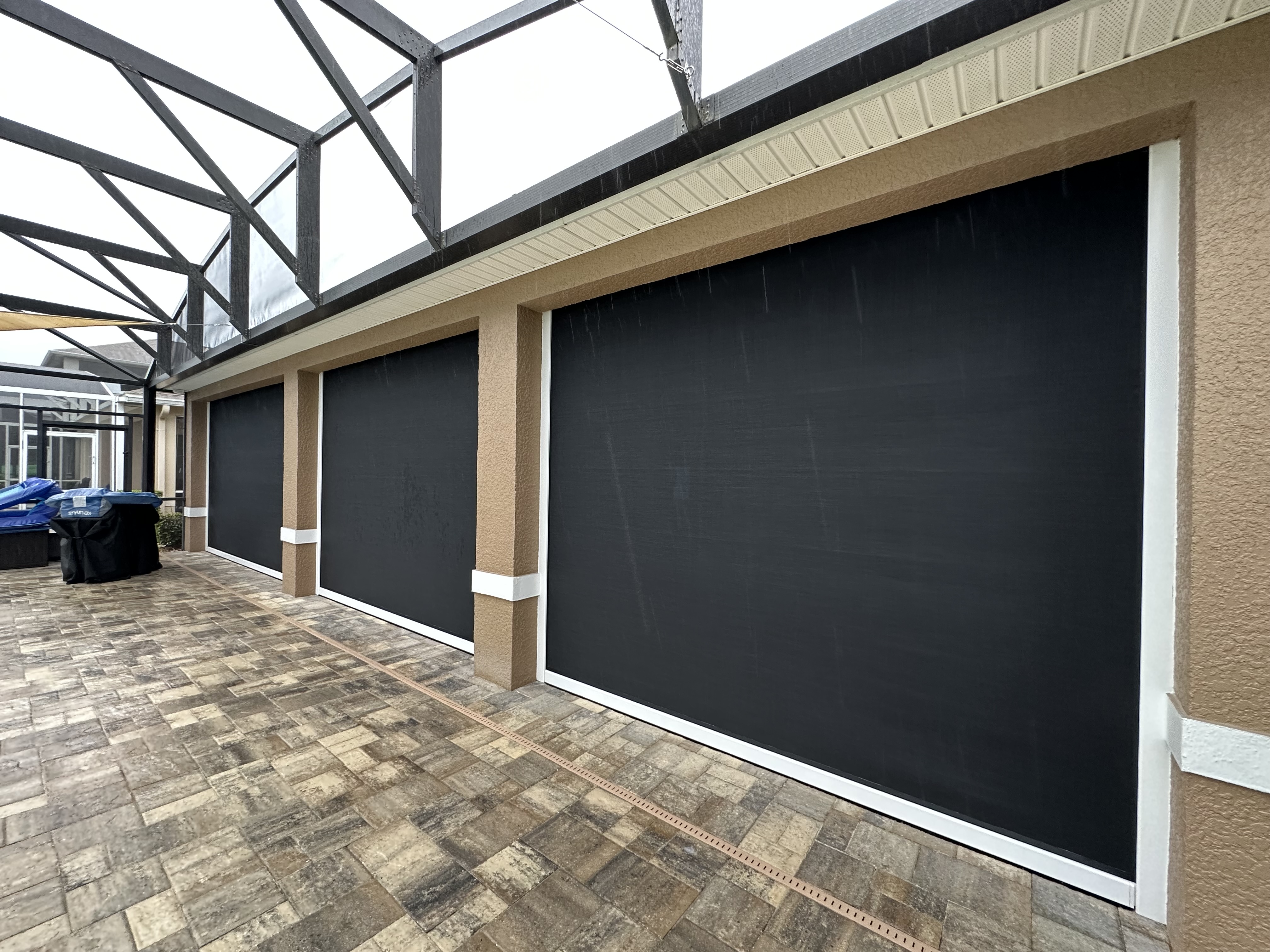 FL Outdoor Functional Living Outdoors,  A photo of Three Motorized Hurricane Defender Screens.  The housing located on the top is white and so are the tracks.  Screens are black. 