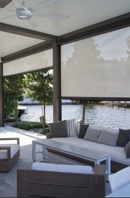 A sofa set position beneath a motorized aluminum pergola. The fame work is gray and the motorized screen white 
