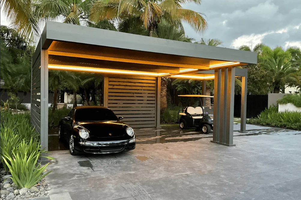 Modern aluminum carport pergola with LED ambient lighting sheltering a luxury car and golf cart surrounded by tropical Florida landscaping