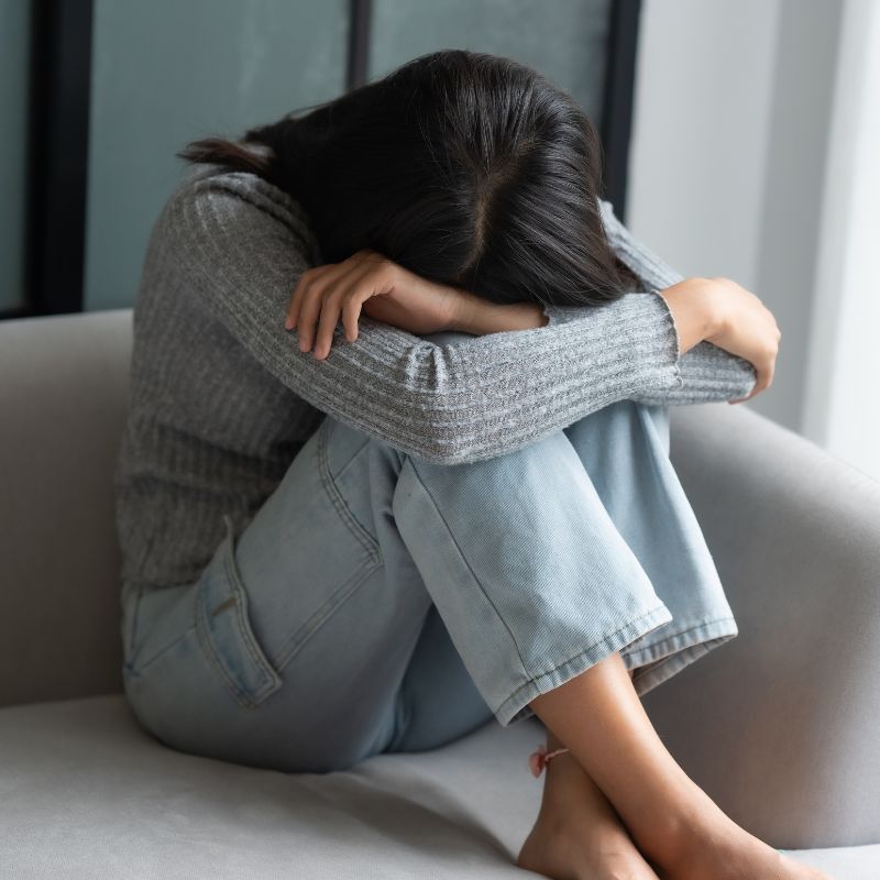 Woman sitting curled up feeling overwhelmed and emotionally stuck, representing inner struggle and lack of clarity