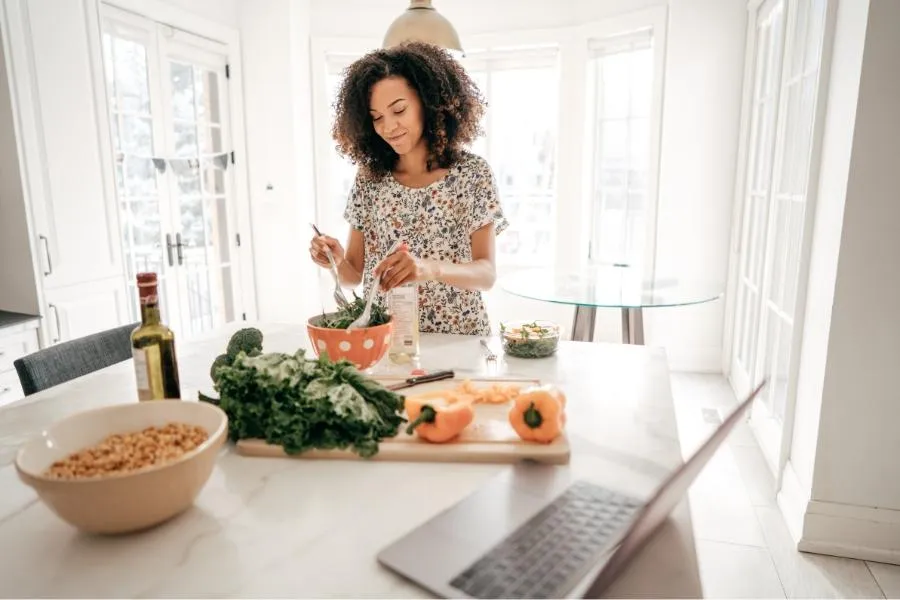 Slim woman mixing a fresh salad in a bright white kitchen, embracing a healthy plant-based lifestyle.