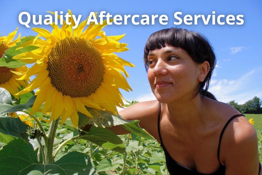 Woman admiring a large sunflower in a summer garden, representing friendly garden aftercare and ongoing support.
