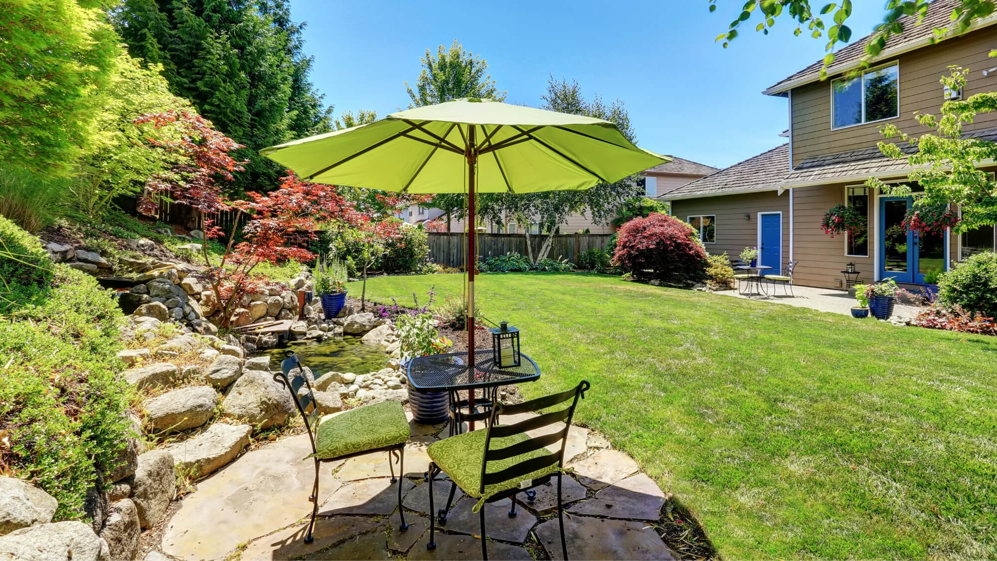 Large garden with reclaimed patio seating area overlooking wildlife pond, lawn and planting