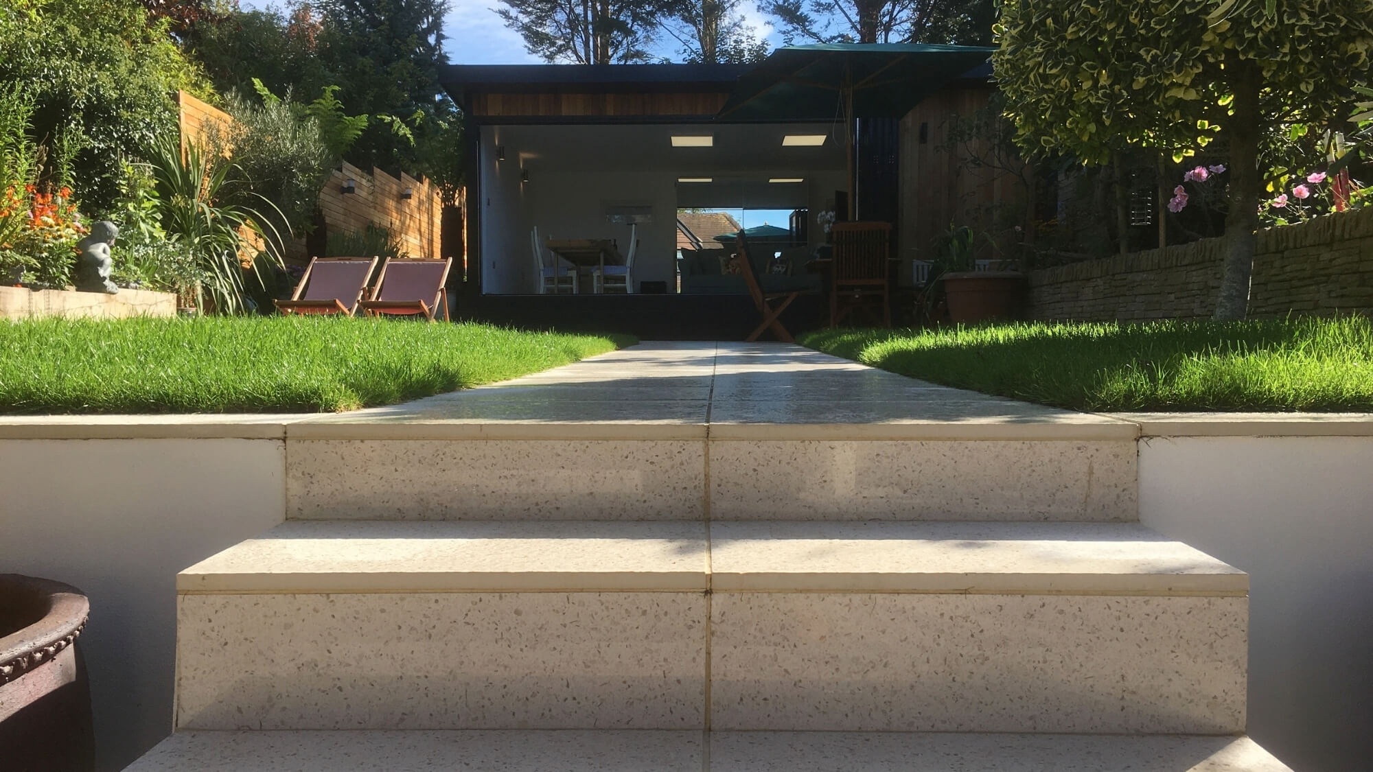 Modern stepped lawn terrace leading to contemporary garden room in Carshalton
