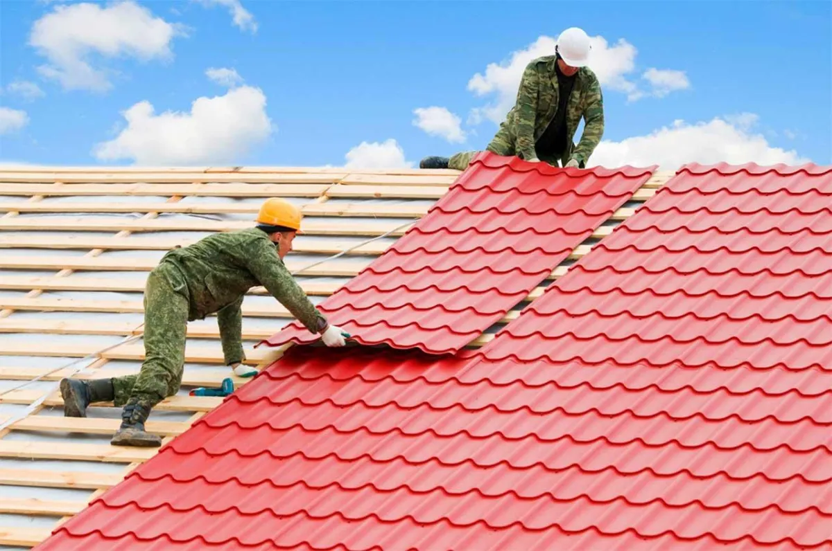Workers installing red metal roofing panels on a house.