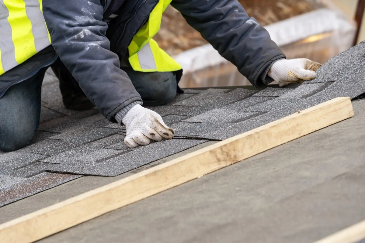 Worker installing asphalt shingles on a roof.