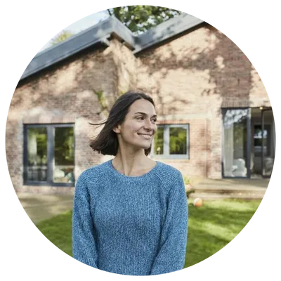 Smiling woman standing outside a brick house wearing a blue sweater.