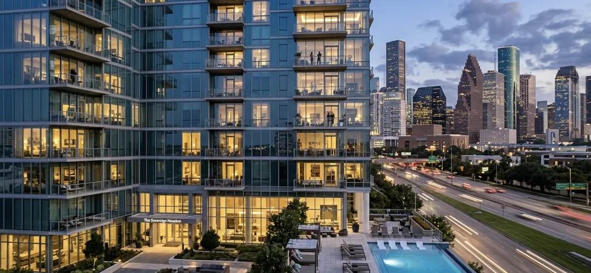A modern luxury high-rise apartment building at twilight with glowing windows, overlooking an illuminated city skyline.