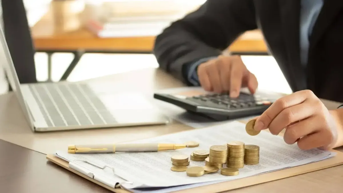 Main manipulant des pièces de monnaie devant un ordinateur, symbolisant l’optimisation des ressources financières grâce à un financement adapté.