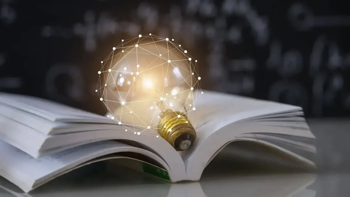 Ampoule posée sur un livre ouvert, symbolisant les guides pédagogiques et conseils pratiques en investissement immobilier.