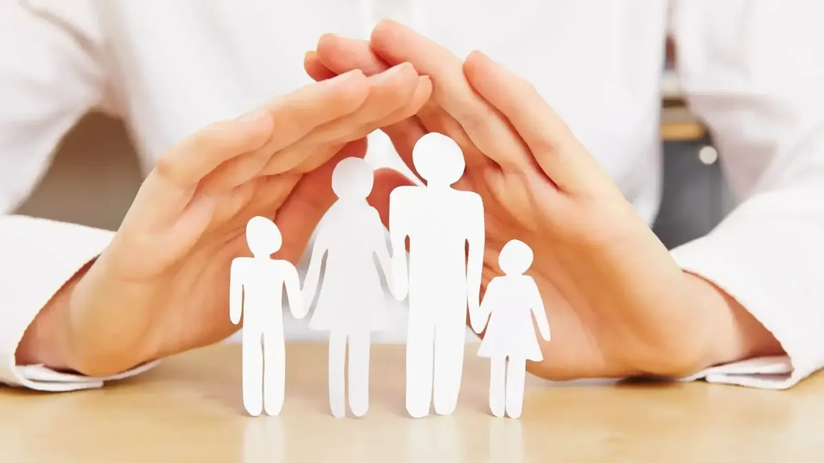 Mains protectrices entourant des figurines représentant une famille, illustrant la protection financière et la prévoyance.