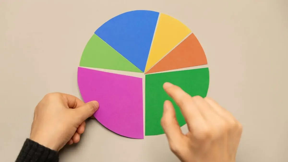 Main tenant un camembert coloré représentant la diversification des placements financiers dans une stratégie de gestion de patrimoine.