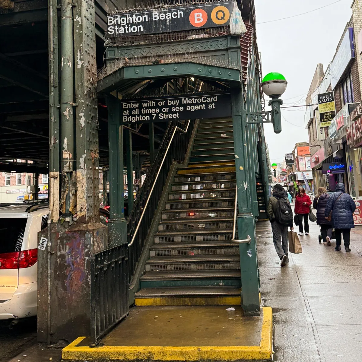 Entrada a la estación Brighton Beach del metro de Nueva York — acceso elevado con escaleras y letreros de las líneas B y Q.
