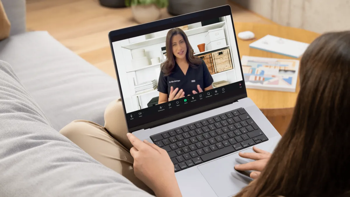 A person holds a laptop showing a virtual consultation with Dr. Hiba speaking on a video call.