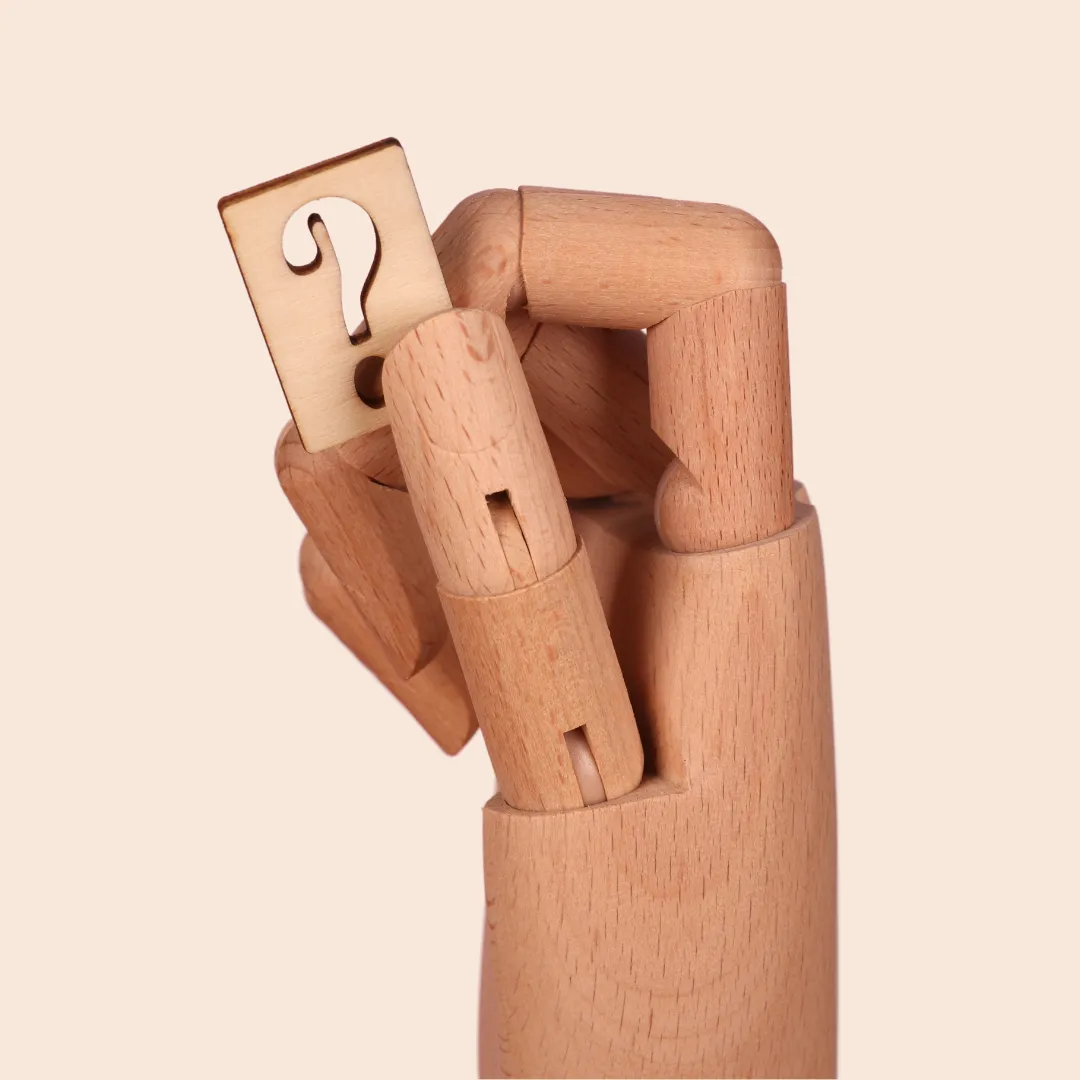 A wooden mannequin hand holding a square block with a question mark cutout.