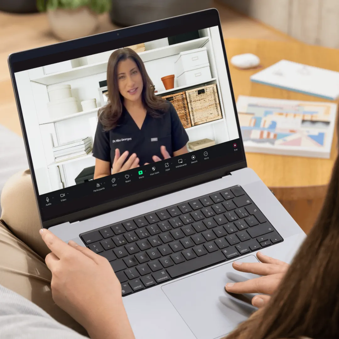 A person holds a laptop showing a virtual consultation with Dr. Hiba speaking on a video call.