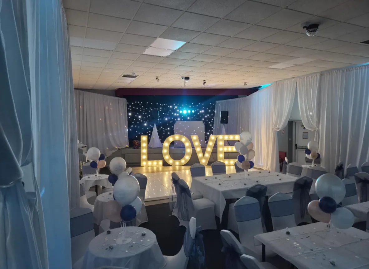 Luxury wedding venue dressing with draping, white chairs and gold sashes.
