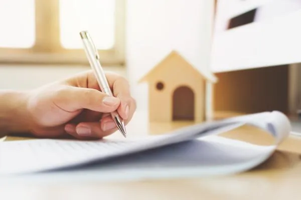 hand writing with pen on paper with tiny wooden house in background