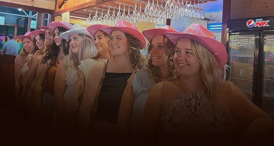 A group of women wearing western hats and enjoying a night out at the bowling alley.