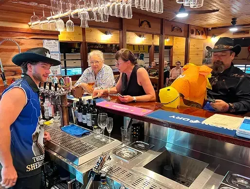 Customers sitting at the rustic saloon bar and ordering drinks from the bartender.