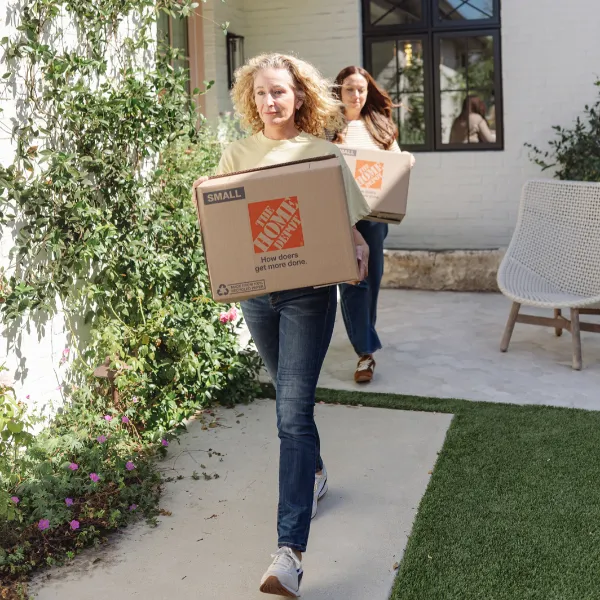 Kaymenity Home move-in team carrying moving boxes along a garden path into a client’s new home