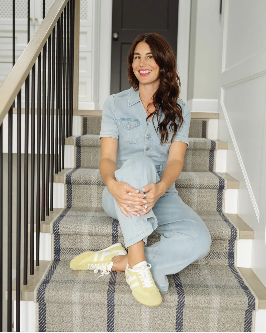 Kaymenity Home founder Ashley sitting on a carpeted staircase in a denim jumpsuit