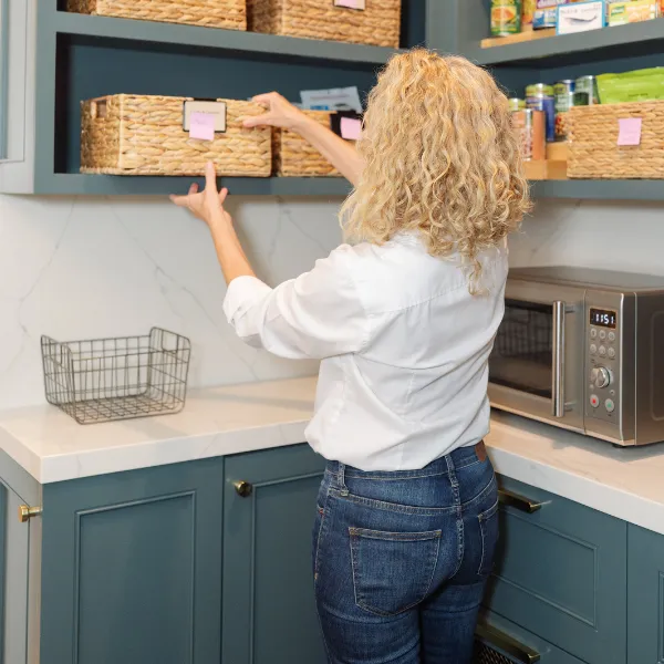 Organizer placing labeled woven baskets on pantry shelves above a marble countertop
