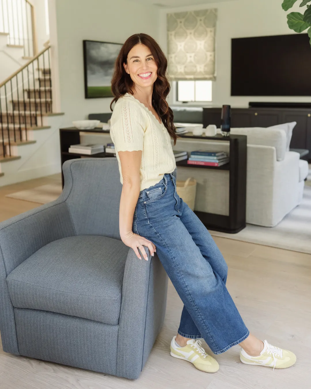 Kaymenity Home founder Ashley leaning on a blue armchair in a bright living room