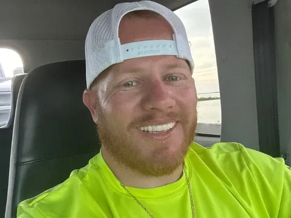 Smiling man in a bright green shirt and white cap, owner of a local trash bin cleaning company.