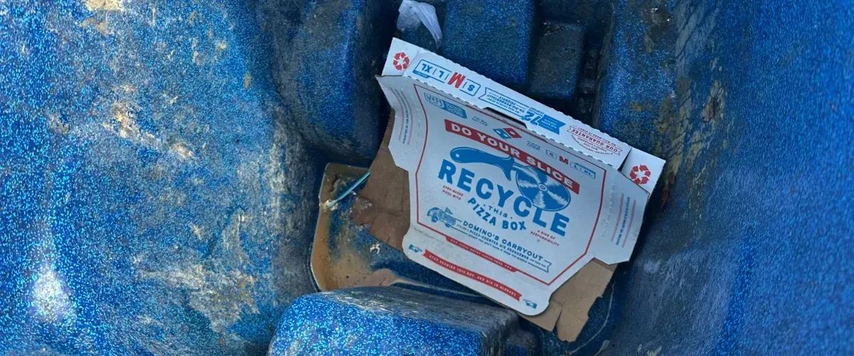 Open pizza box sitting in a recycling bin with visible buildup on the walls.