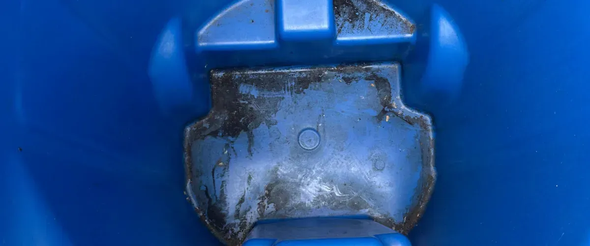 Dirty and stained bottom of a blue trash bin before cleaning.
