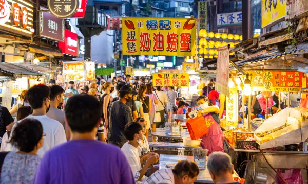 A vibrant Asian night market bustling with people, colorful signs in Chinese, and food vendors serving local street food under glowing lanterns – capturing the lively atmosphere and sensory excitement of Asia.